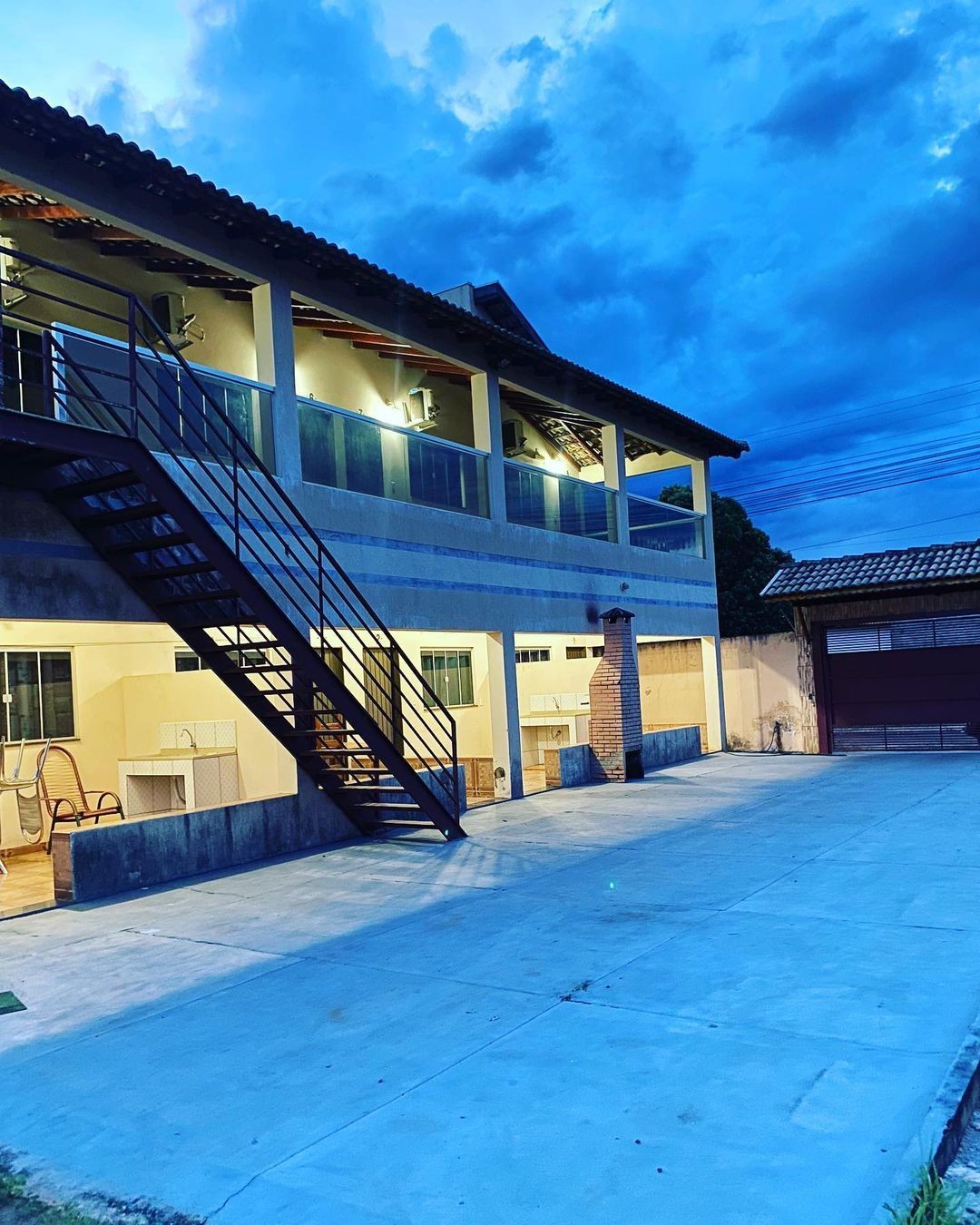 Two-story building at dusk with outdoor staircase, lights on, and cloudy evening sky.