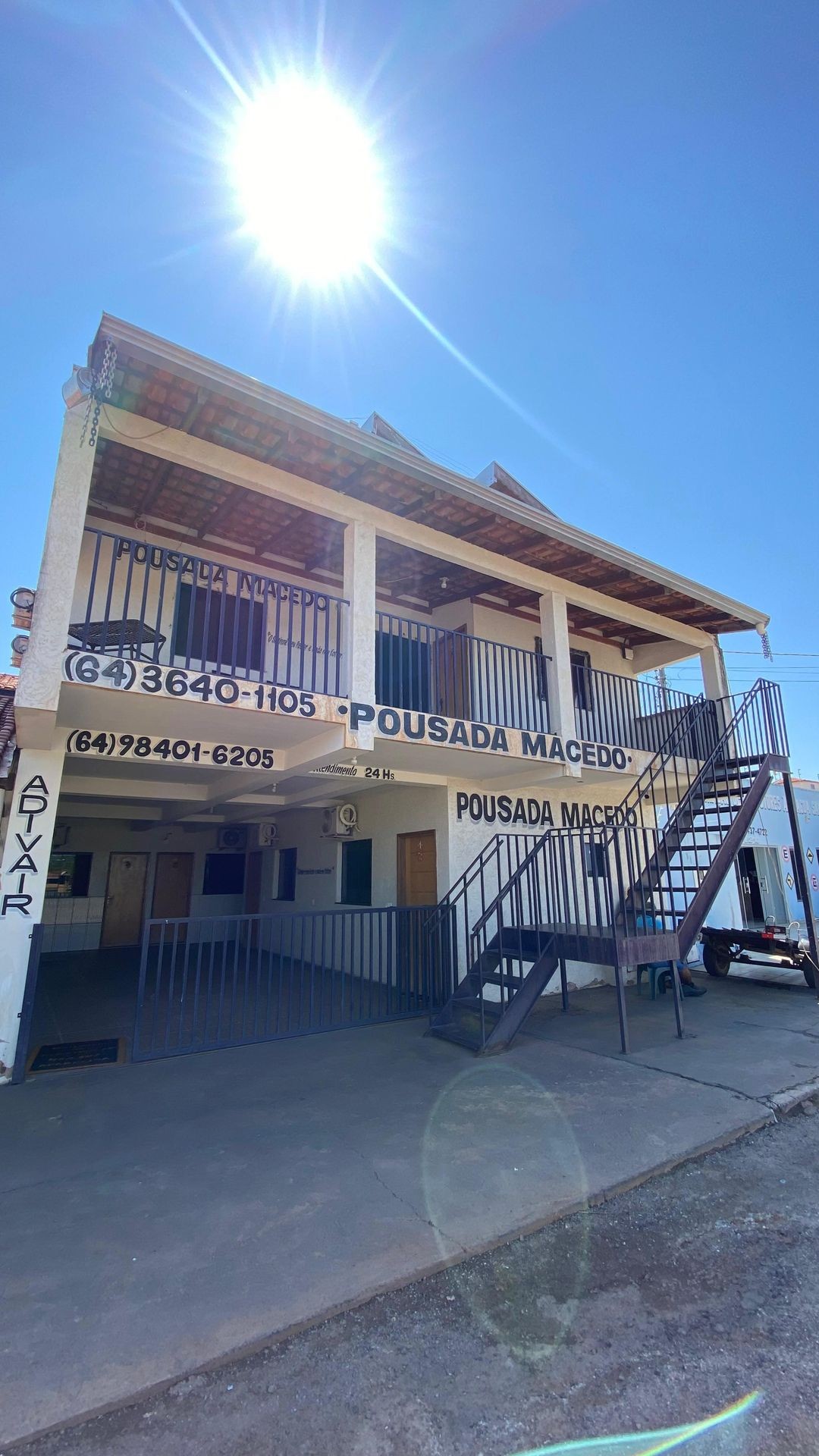 Two-story building under bright sunlight with a staircase and visible signage for Pousada Macedo.